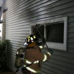 Captain Jimmy Taylor breaks a window to provide smoke ventilation for the crew inside the structure.